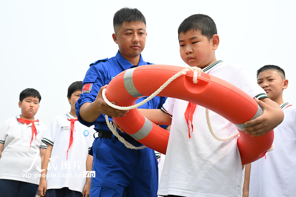 2026年7月3日，山东青岛即墨区环秀中心小学，蓝天救援队队员为学生讲解救生圈的正确使用方法。山东青岛即墨区环秀中心小学邀请即墨区蓝天救援队队员走进校园，开展暑期防溺水安全教育。救援人员通过现场教授防溺水安全知识与救生技能，增强学生的暑期安全防范意识，提高应急自救互救能力。张涛摄（人民图片网）
